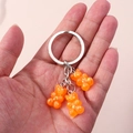 Detail of three orange glitter resin gummy bear charms on a silver metal keychain - Orange