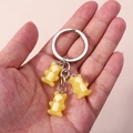 Detailed view of three yellow translucent skeleton bear keychains held in palm - Yellow