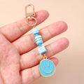 Close-up of blue beaded smiley face keychain with gold metal clasp and striped beads - Blue