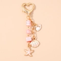 Detalle de llavero dorado con cierre de corazón y dijes de ballena y concha con perlas rosa - Rosa (Estrella de Mar Rosa)