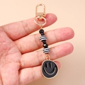 Handheld view of a trendy beaded smiley face keychain with black and gold beads on pink base - Black