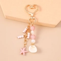 Detail of starfish and shell charms on a gold heart keychain with pink beads - Pink Shell Starfish