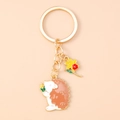 Detail of cute hedgehog keychain with golden ring holding a yellow corn charm - Flower Hedgehog