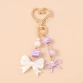 Close-up of a pearl bow keychain with purple striped beads and golden heart clasp - Purple