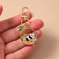 Détails d'un porte-clés panda doré avec du bambou vert et des breloques de fleurs roses - Panda aux Fleurs de Prunier