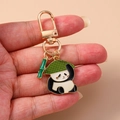 Porte-clés panda doré avec chapeau de feuille verte et breloque bambou tenu à la main - Panda Bambou Chapeau de Paille