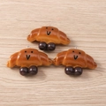 Macro view of three realistic croissant charms with cute faces and silver metal hooks - Cartoon Smile Croissant / Set of 4