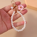 Dettaglio di fiore di ciliegio in smalto rosa e perle bianche su portachiavi dorato - Rosa