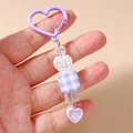 Détail d'un porte-clés cœur violet avec perle à carreaux et breloques de sac - Violet