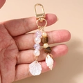 Detail of ocean-themed beaded keychain featuring white seashells and golden metal clasp - Conch Shell Beaded Style