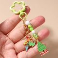 Détail d'un porte-clés de Noël perlé avec breloque sapin vert et lettres dorées sur fond beige - Sapin de Noël Perlé Lettre