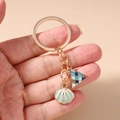 Close-up of golden keychain with blue shell and geometric triangle enamel pendants - Shell Triangle Keychain