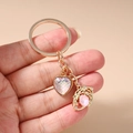 Detalle de un llavero dorado de corazón y estrella con textura irisada en la mano - Llavero de Ojo de Corazón Rosa