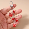 Detail of hand holding silver keychain with three red paw charms and small bells - Red Paw Print Keychain