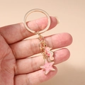 Primer plano de un llavero dorado con dijes de caballito de mar y estrella de mar rosa - Llavero de Estrella de Mar y Caballito de Mar