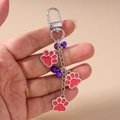 Close-up of silver paw print keychain with red enamel charms and small purple bells - Rose Red Paw Print Keychain