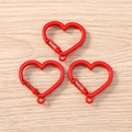 Primo piano di moschettoni a molla a forma di cuore rosso su una superficie di legno - Rosso