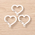Tre moschettoni bianchi a forma di cuore su sfondo di legno chiaro per accessori fai da te - Bianco