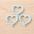 Tre moschettoni a forma di cuore azzurro con chiusura a molla su fondo in legno - Blu