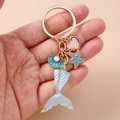 Detail of mermaid tail heart keychain with starfish and shell charms held in hand - Light Blue Fish Tail