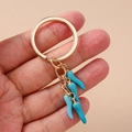 Detailopname van een modieuze sleutelhanger met vier chilihangers en een gouden ring - Meerblauwe Chilipeper