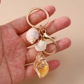 Detail of beach shell keychain with golden lobster clasp held against pink background - Yellow Conch