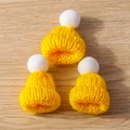 Close-up of three yellow knitted mini hats with white pom-poms on a wooden background - 10 Pieces/Pack / Yellow