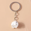 Close-up of a 3D white elephant keychain with a silver metal ring on a pink background - White