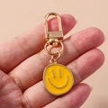 Detalle de llavero metálico con cara sonriente amarilla y cierre de mosquetón dorado - Amarillo