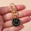 Primer plano del llavero de carita sonriente dorada con colgante de esmalte negro - Negro