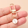 Close-up of golden letter I charm with white enamel on a polished lobster clasp keychain - White Letter I
