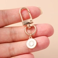 Close-up of golden letter O keychain with white enamel charm held by hand - White Letter O