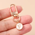 Detail of rose gold keychain with enamel letter F charm held in hand with pink background - White Letter F