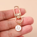 Macro shot of gold lobster clasp and white enamel round pendant with letter H - White Letter H