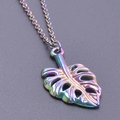 Gros plan sur un pendentif feuille de monstera en acier inoxydable aux reflets arc-en-ciel - Set de colliers / Arc-en-ciel