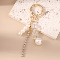 Detail eines eleganten goldenen Schlüsselanhängers mit Perlen, Perleffekten und Strasssteinen - Perle Strass Kette Stil
