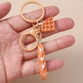 Detail of creative waffle and baguette keychain held by hand featuring lifelike bread texture - Flesh Color Baguette Triangle