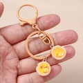 Détail des breloques œufs au plat en résine sur un porte-clés en métal jaune tenu en main - Tarte aux Œufs Couleur Chair