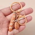Close-up of realistic resin bread and baguette keychain pendants held in hand - Flesh Color Baguette