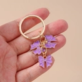 Elegante llavero dorado con tres lazos de esmalte púrpura para decorar bolsos de mano - Morado