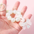 Iridescent beaded keychain with pearl bow and flower charms held in hand on pink background - Green