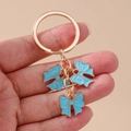 Llavero dorado con tres colgantes de lazo en esmalte azul cielo en la mano - Azul