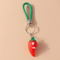 Makroaufnahme eines lustigen roten Chili-Schlüsselanhängers mit Gesicht und grünem Band - Lustige Chili / Rot