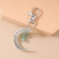 Detail of silver crescent moon keychain with green stones on a geometric stand - Light Green Stone Moon