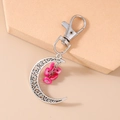 Close-up of crescent moon keychain with silver hollow design and pink stones on stone slab - Rose Red Stone Moon