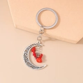 Detail of silver hollow moon keychain featuring vibrant red stones on a beige background - Red Stone Moon