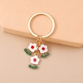 Dettaglio portachiavi floreale dorato con petali bianchi e foglie verdi su supporto - Bianco