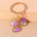 Détail de trois pendentifs en cœur avec émail violet et finitions pailletées dorées - Cœur Tai Chi Violet