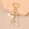 Detail view of pearl bow keychain with heart clasp on elegant display pedestal - Gold Bowknot