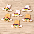 Makro-Detail von sechs Emaille-Bär- und Regenbogen-Anhängern auf hellem Holz - 10er Pack / Gemischte Regenbogenbären